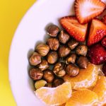 Close-up of a bowl with fresh fruits and nuts against a vibrant yellow backdrop.